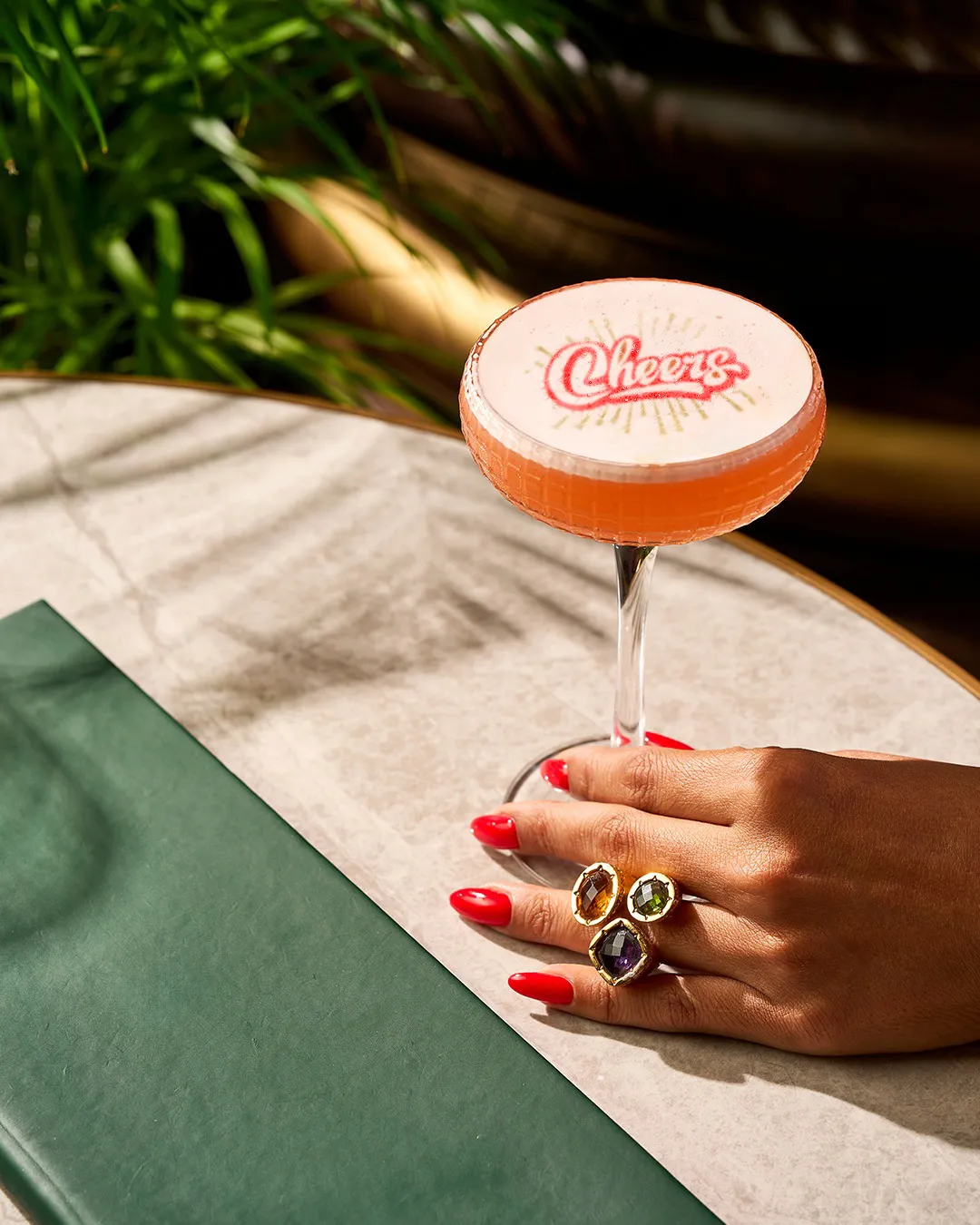 Cocktail printer result with 'Cheers' text on cocktail foam, next to a green table setting