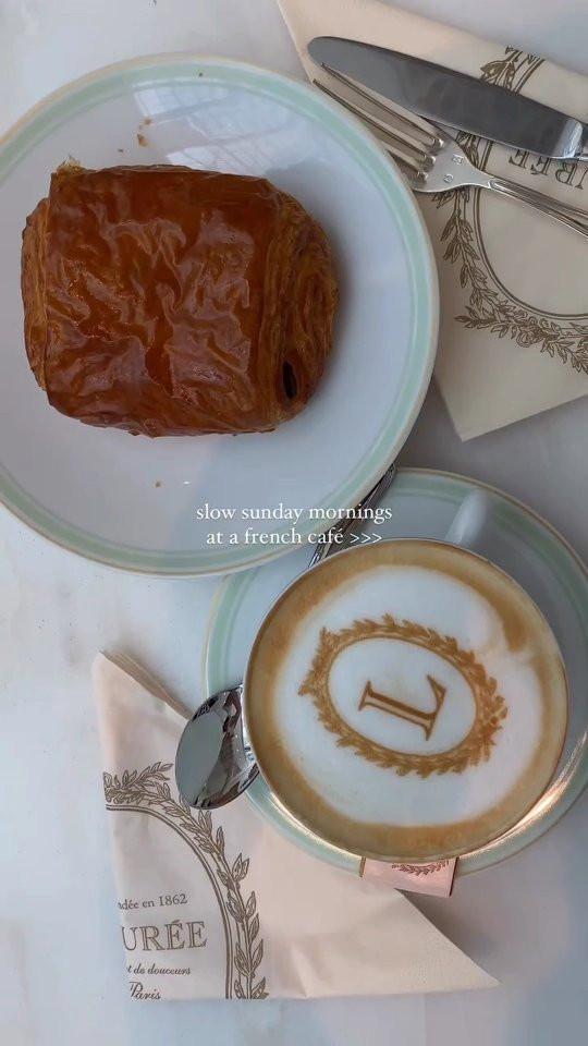 Latte art yazıcısı ile latte köpüğüne L harfi işlenmiş kahve, yanında kruvasan